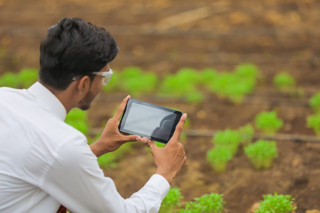 technology and people concept, young indian agronomist using tablet or smartphone at greenhouse
